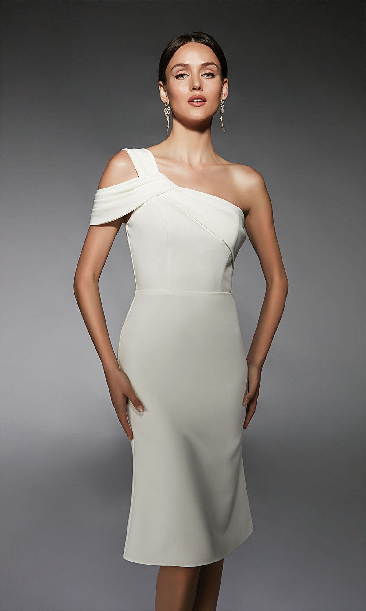 A woman models the Alyce 70054 knee-length semi-formal dress in ivory, featuring draped detailing and a one-shoulder design, against a plain gray background.